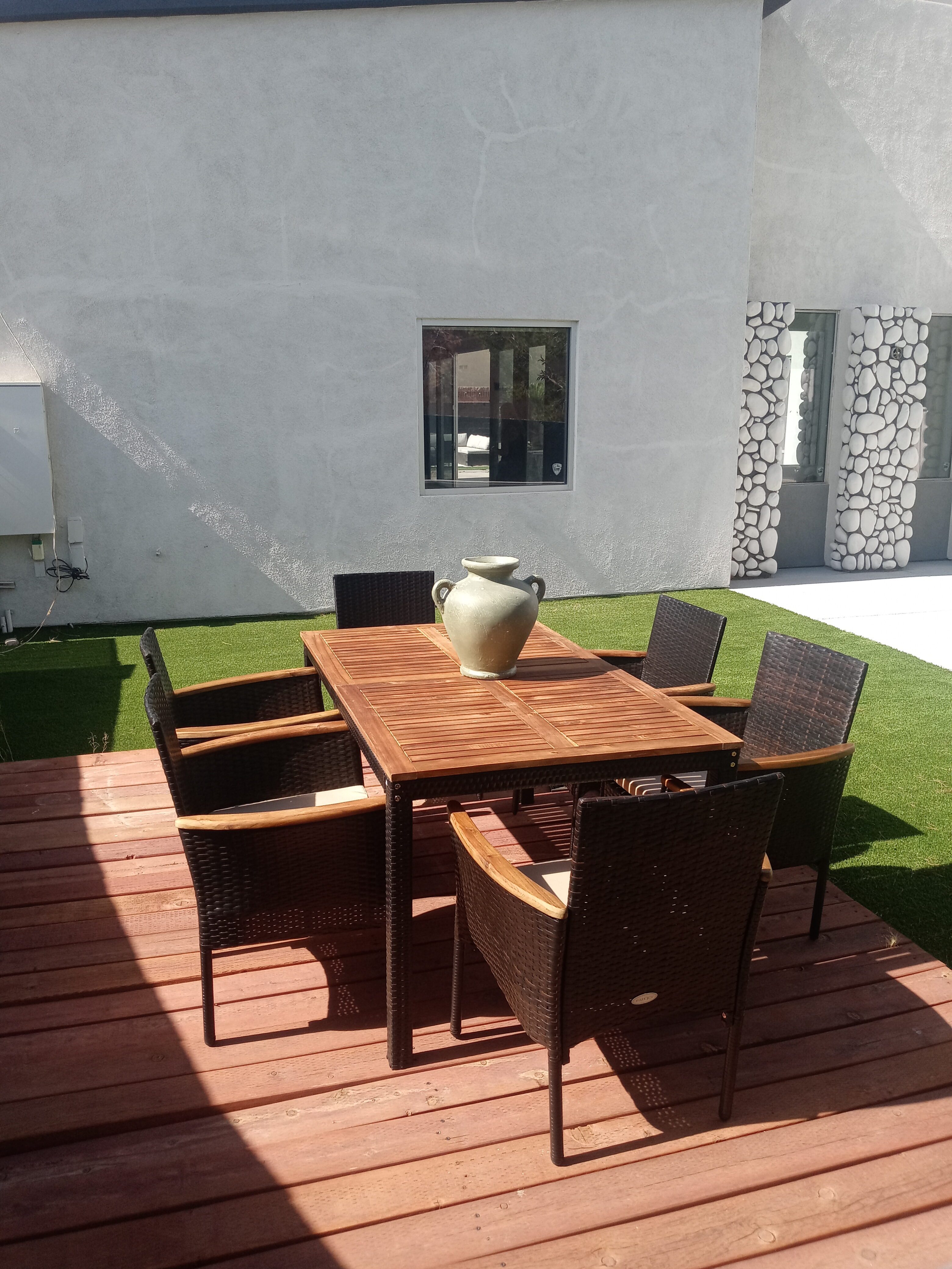 Elegant indoor dining area featuring black woven chairs with wooden armrests, a modern white table, and a poolside view through large glass doors.